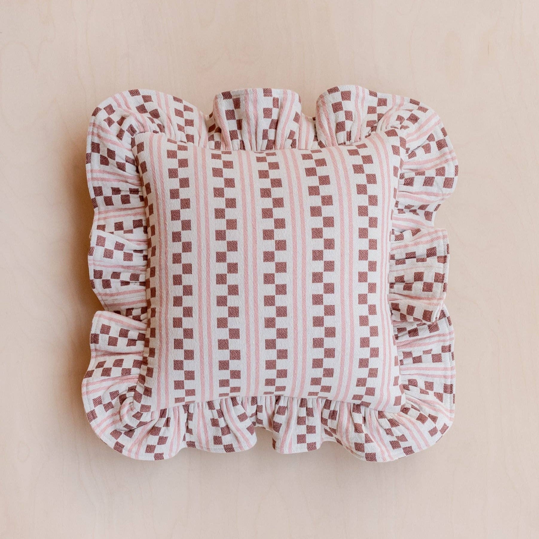 Pink Checkered  and striped cushion with ruffled trim on a beige background