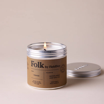 Candle in a 'Folk by Field Day' jar with a lit wick on a beige background